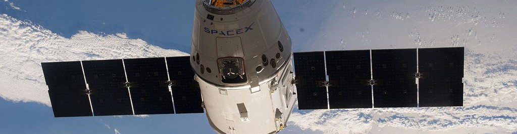 dragon capsule with solar panels extended above Earth's surface