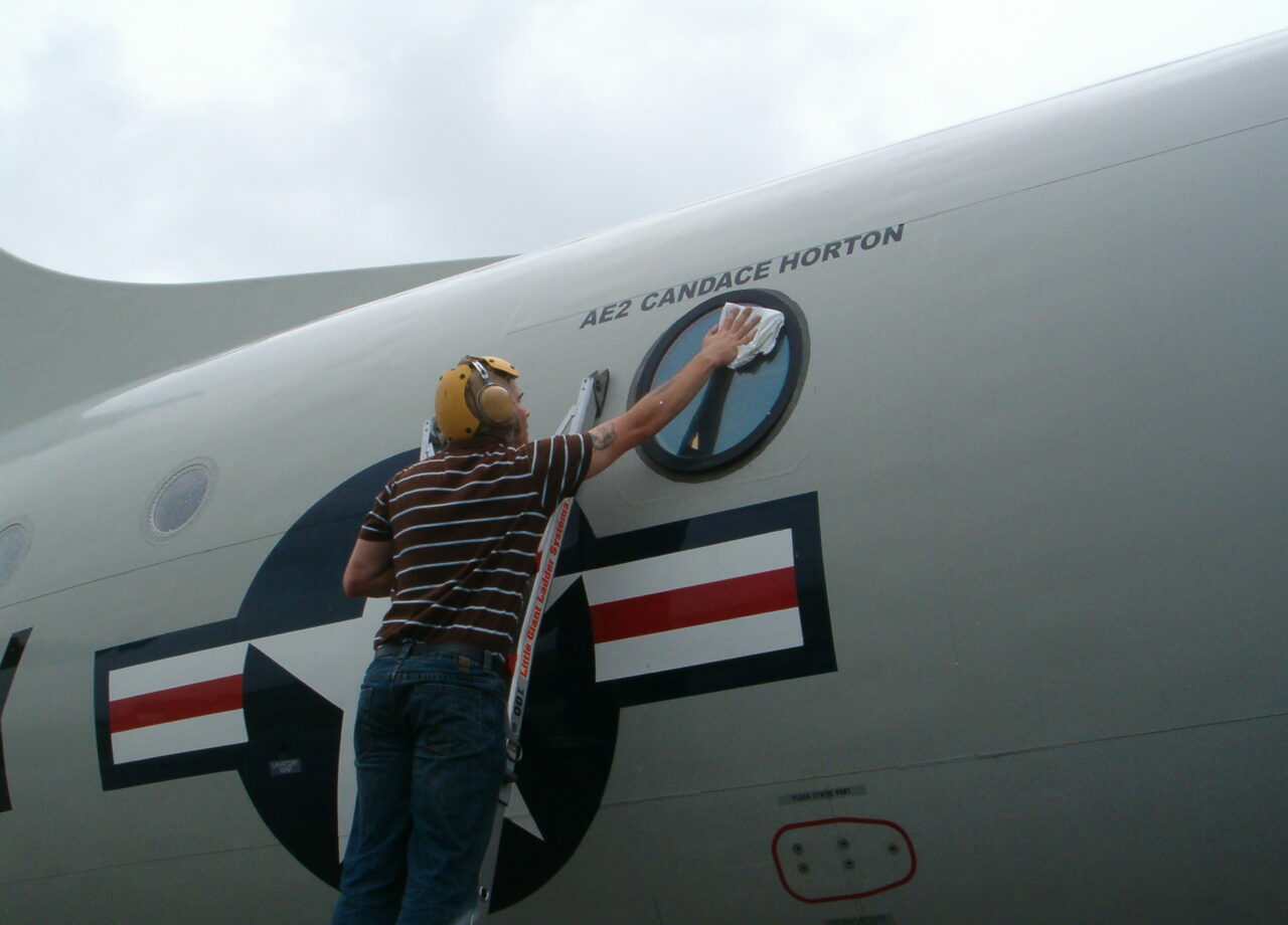 Member of the cast glance Navy P-3 crew polishing the viewing window on the aircraft