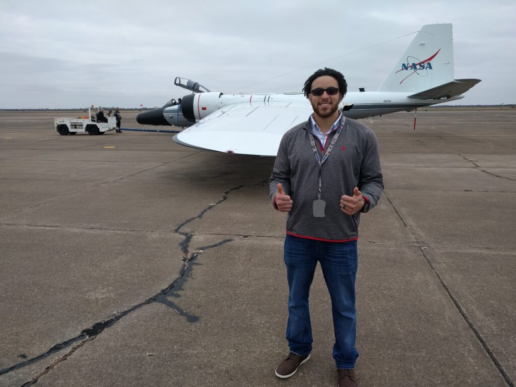 Carey Scott, Principal Investigator, standing in front of the WB-57 jet with two thumbs up.