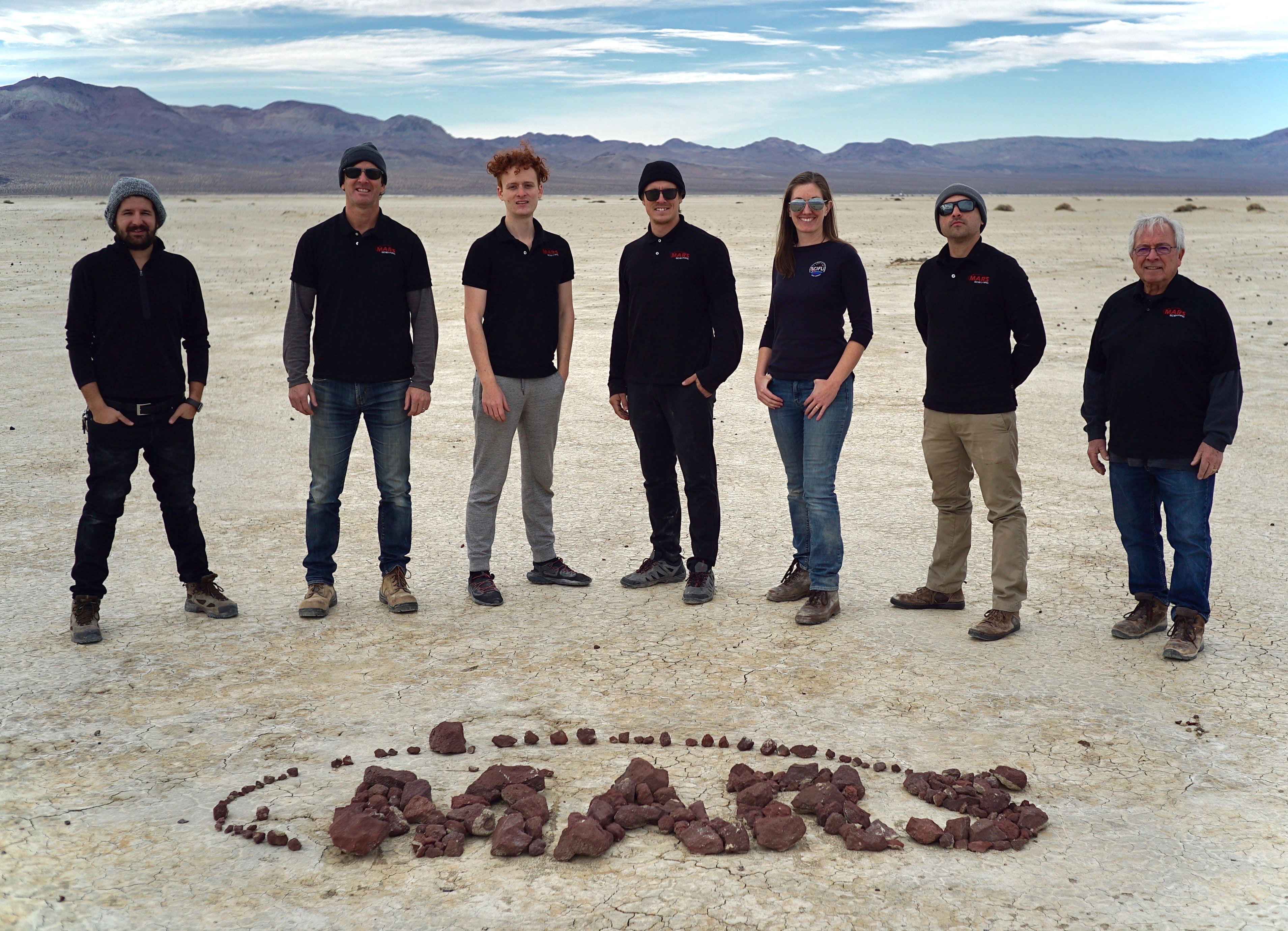 The MARS team and Dr. Jennifer Inman (project manager for SCIFLI) stand in a desert landscape. The MARS logo is made with rocks on the ground in front of them.