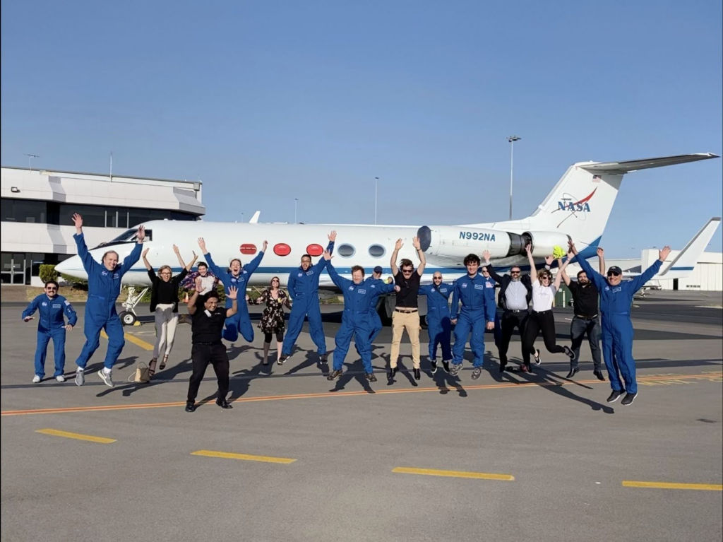 The SCIFLI team and their partners jump in the air in front of a jet.