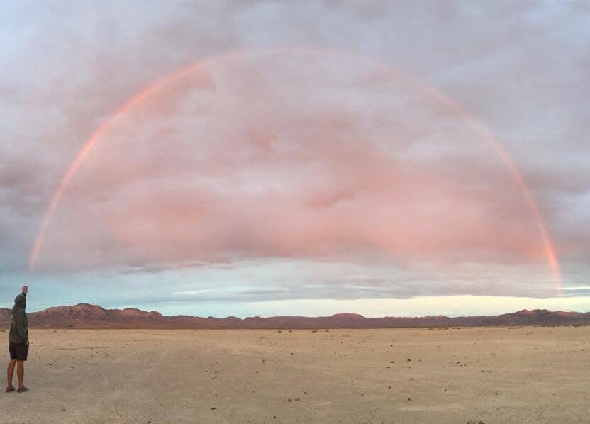 Someone takes a picture of a full rainbow in a deserted desert landscape.