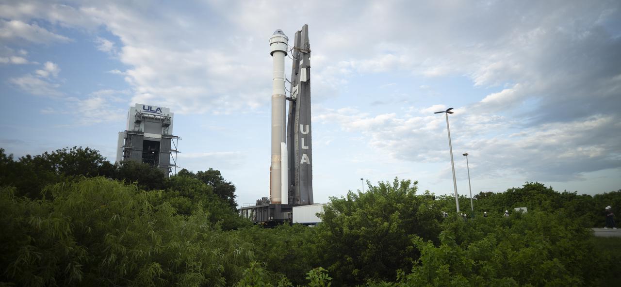A rocket, topped with a Boeing capsule, on a launchpad. The support for the rocket has the letters ULA.